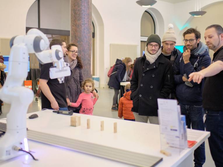 Menschen blicken auf einen kleinen Industrieroboter.